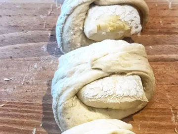 Drei Stücke Teig sind auf einem Holzbrett gewickelt.
